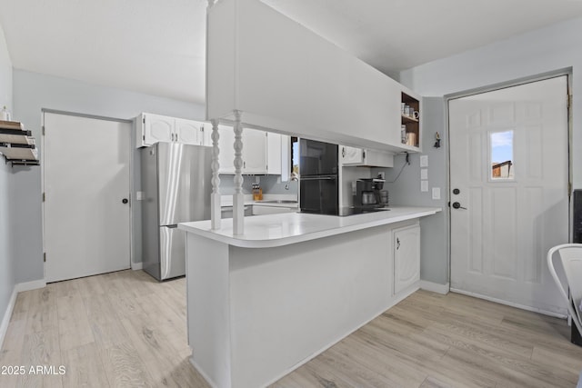 kitchen with light countertops, freestanding refrigerator, white cabinets, a sink, and a peninsula