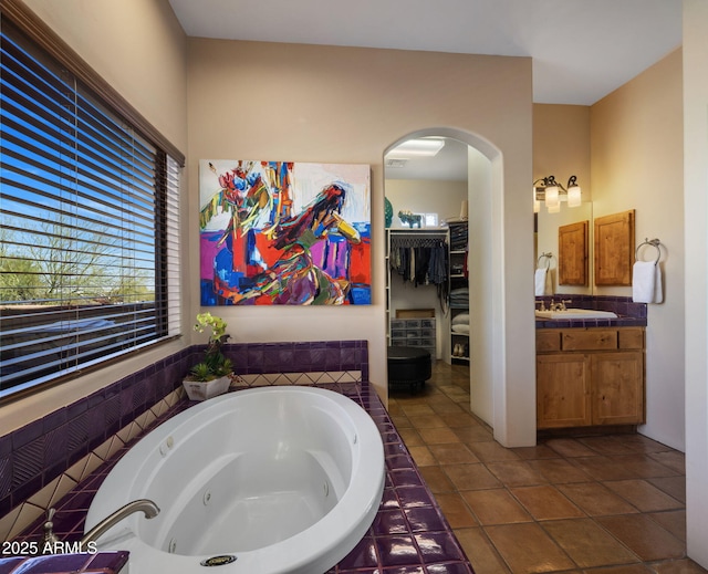 bathroom with tile patterned floors, a spacious closet, a tub with jets, and vanity