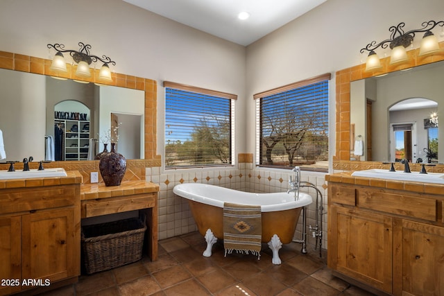 bathroom with two vanities, a freestanding bath, a sink, wainscoting, and tile walls