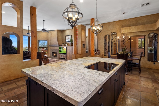 kitchen featuring visible vents, open floor plan, a lit fireplace, ceiling fan with notable chandelier, and black electric cooktop