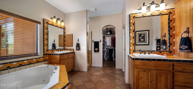 full bath with a jetted tub, two vanities, a spacious closet, and a sink