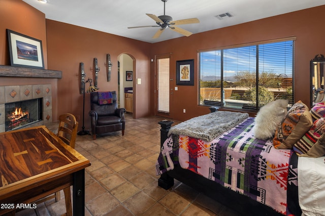 bedroom featuring arched walkways, visible vents, a tile fireplace, and a ceiling fan