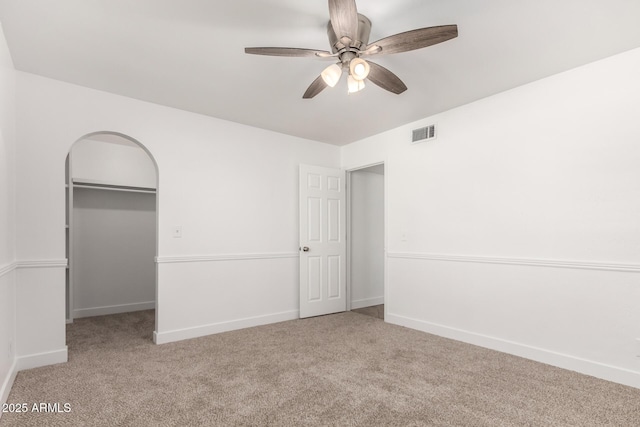 unfurnished bedroom featuring a closet, visible vents, arched walkways, and carpet flooring