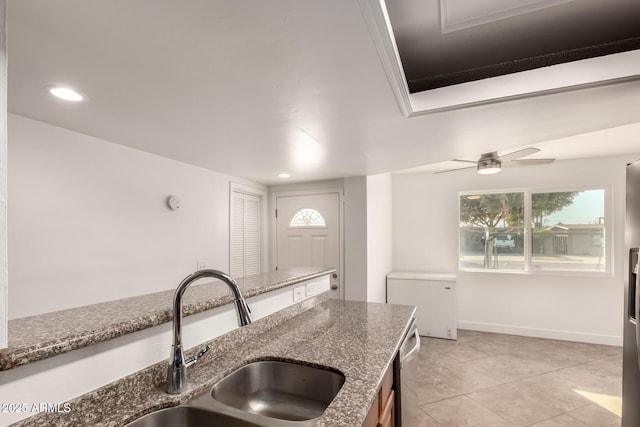 kitchen with light tile patterned floors, stone counters, refrigerator, a sink, and baseboards