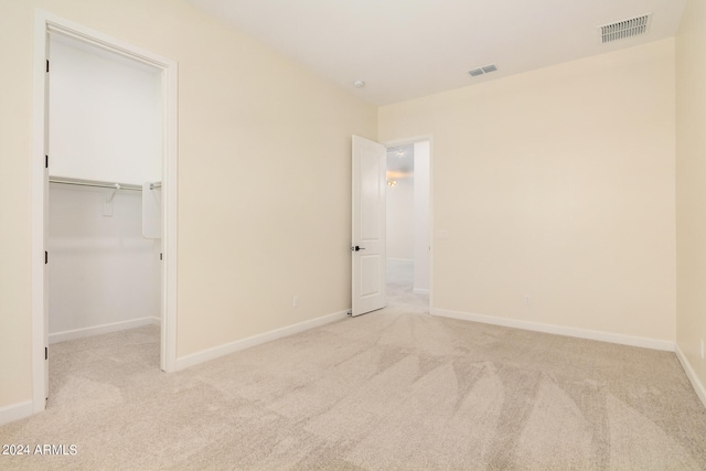 unfurnished bedroom with a walk in closet, light colored carpet, and a closet