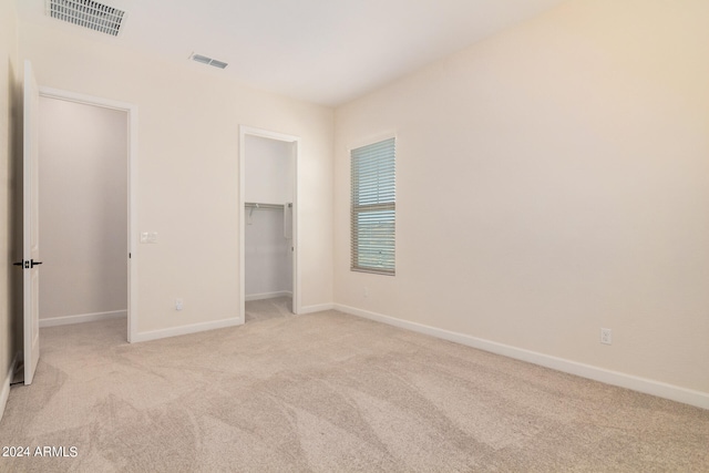 unfurnished bedroom featuring a spacious closet, light colored carpet, and a closet