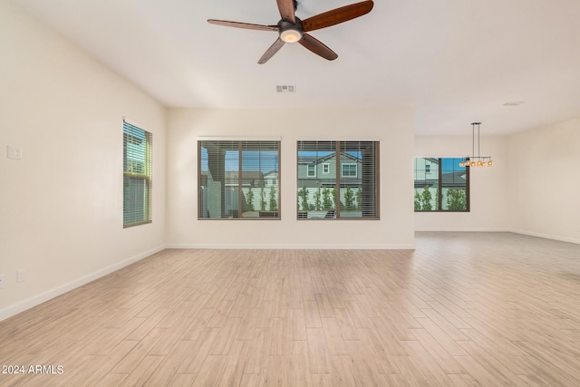 unfurnished living room featuring ceiling fan with notable chandelier and light wood-type flooring