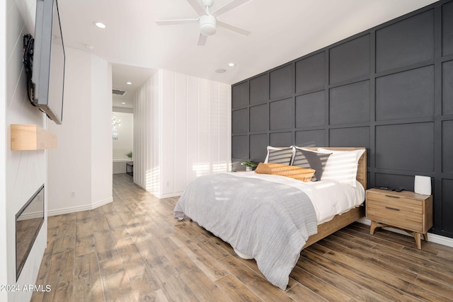 bedroom with a ceiling fan, a decorative wall, wood finished floors, and recessed lighting