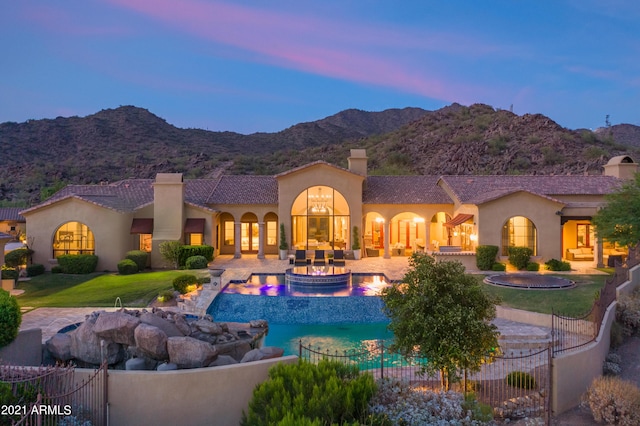 pool at dusk with a mountain view, an outdoor living space, a patio area, and a lawn