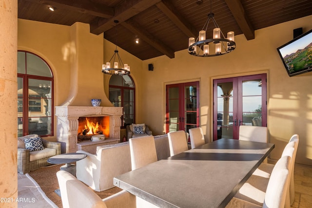 dining space featuring a large fireplace, french doors, beamed ceiling, and an inviting chandelier