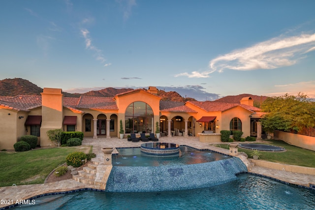 pool at dusk featuring an in ground hot tub, a yard, pool water feature, and a trampoline