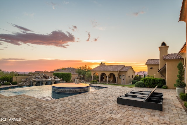 pool at dusk featuring pool water feature, a patio, and an in ground hot tub