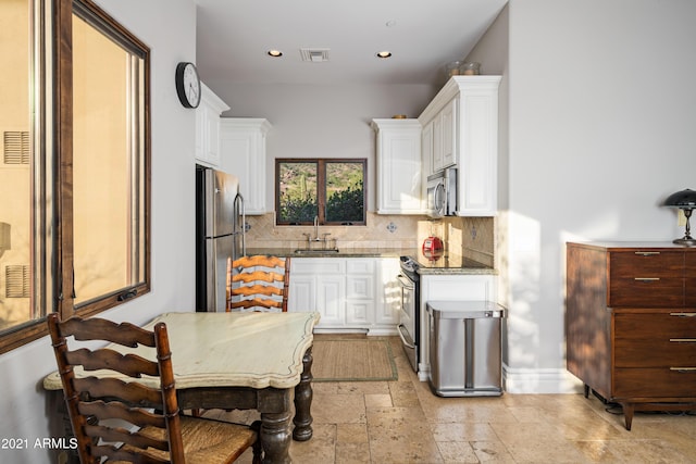 kitchen with light stone countertops, appliances with stainless steel finishes, tasteful backsplash, sink, and white cabinetry