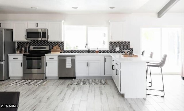 kitchen with a healthy amount of sunlight, a breakfast bar, white cabinets, and appliances with stainless steel finishes