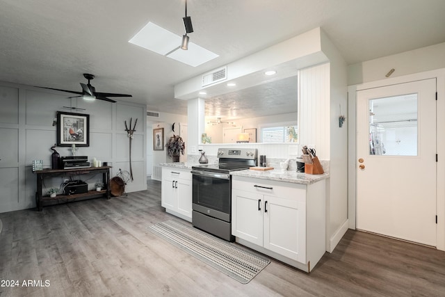 kitchen featuring a skylight, light stone countertops, ceiling fan, stainless steel range with electric cooktop, and white cabinets