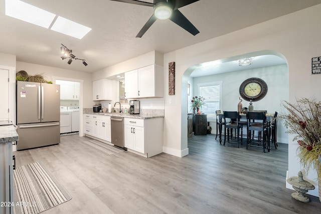 kitchen featuring white cabinets, light wood-type flooring, stainless steel appliances, and washer and clothes dryer