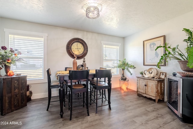 dining space with wood-type flooring, a textured ceiling, and wine cooler