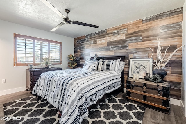 bedroom featuring a textured ceiling, ceiling fan, wood walls, and dark wood-type flooring