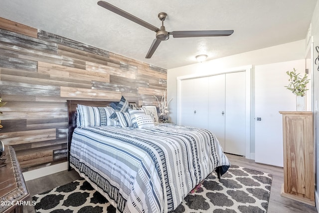 bedroom featuring a closet, hardwood / wood-style flooring, ceiling fan, and wooden walls