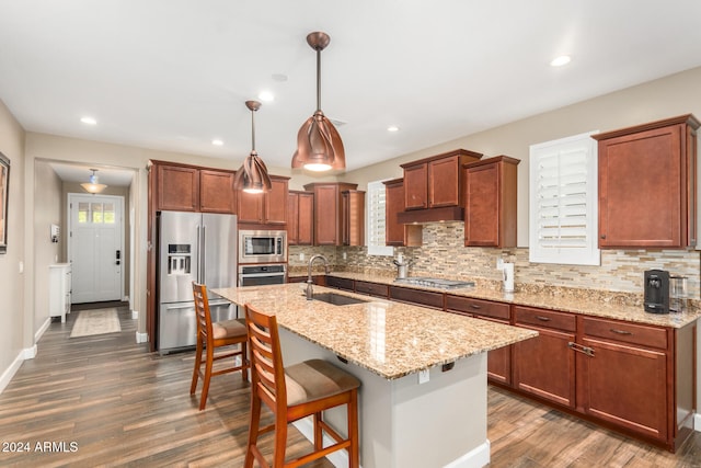 kitchen with sink, hanging light fixtures, stainless steel appliances, dark hardwood / wood-style floors, and a center island with sink