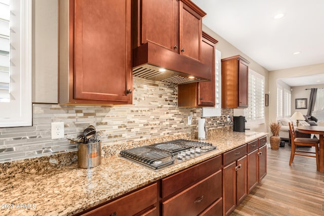 kitchen featuring light stone countertops, light wood-type flooring, stainless steel gas stovetop, and backsplash