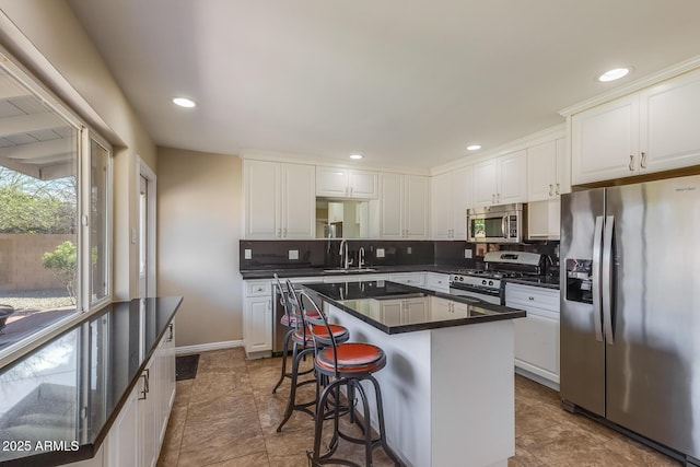 kitchen with stainless steel appliances, tasteful backsplash, dark countertops, and white cabinets