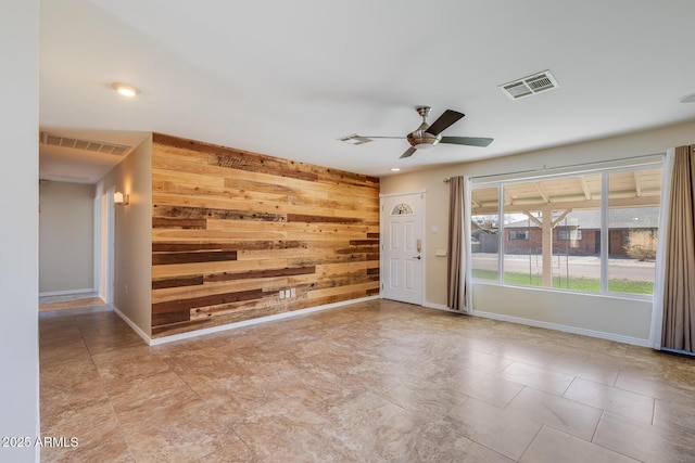 spare room with visible vents, wooden walls, an accent wall, and a ceiling fan