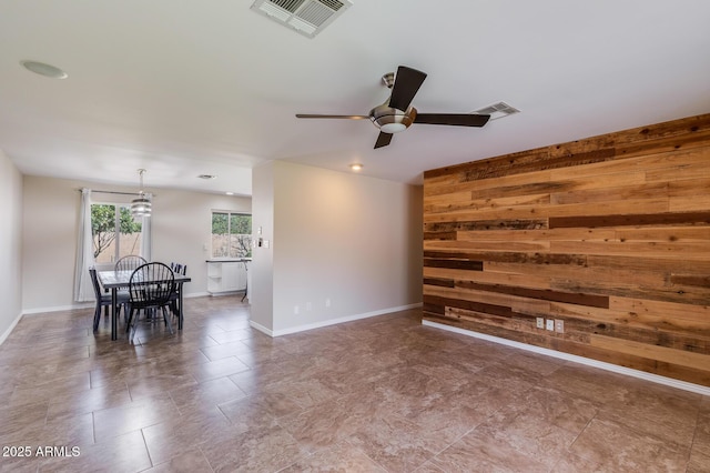 empty room featuring an accent wall, visible vents, wood walls, and ceiling fan