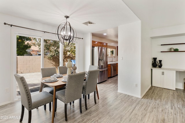 dining area with light wood-type flooring, a notable chandelier, and sink