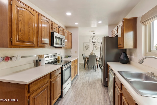 kitchen featuring appliances with stainless steel finishes, sink, decorative light fixtures, light hardwood / wood-style flooring, and an inviting chandelier