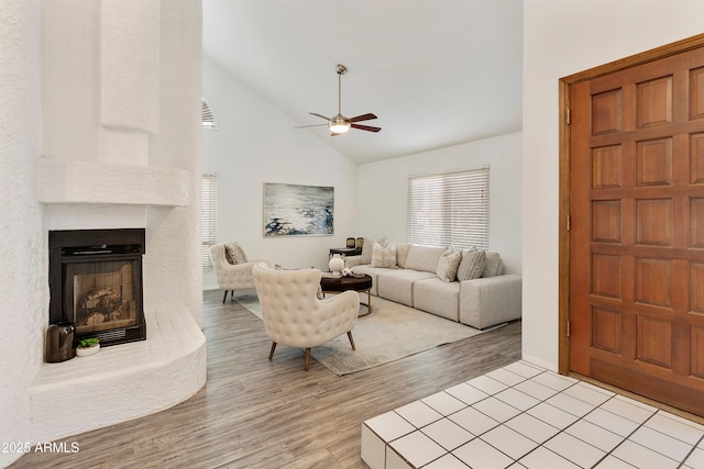 living room featuring ceiling fan, a large fireplace, high vaulted ceiling, and light hardwood / wood-style flooring