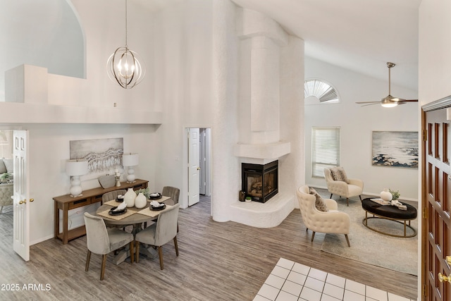 dining area featuring a multi sided fireplace, hardwood / wood-style floors, ceiling fan with notable chandelier, and high vaulted ceiling