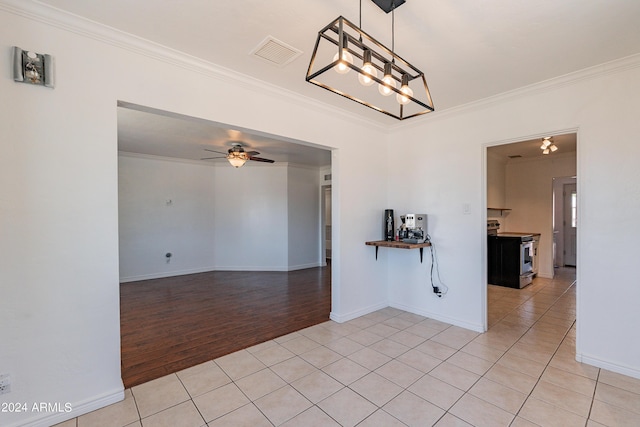 tiled empty room with ceiling fan with notable chandelier and ornamental molding