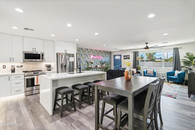 kitchen featuring appliances with stainless steel finishes, light hardwood / wood-style flooring, a kitchen island with sink, and white cabinets