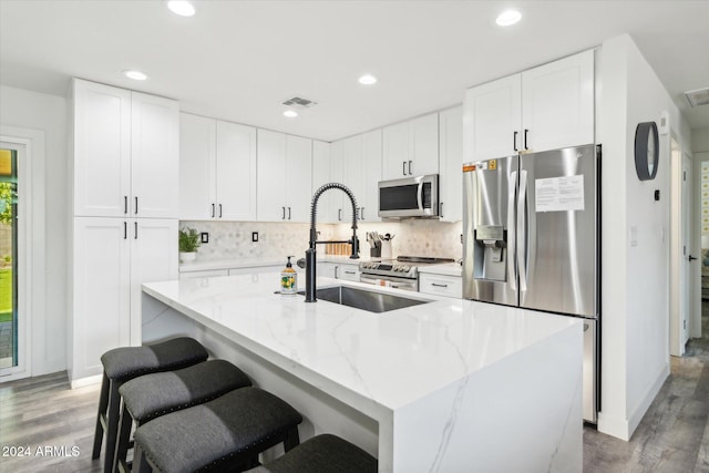 kitchen featuring white cabinetry, appliances with stainless steel finishes, wood-type flooring, and an island with sink