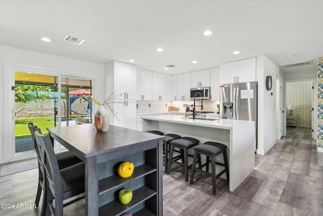 kitchen featuring appliances with stainless steel finishes, a kitchen bar, hardwood / wood-style floors, white cabinets, and a kitchen island with sink