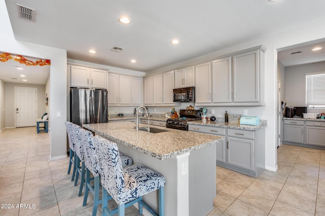 kitchen with gray cabinets, sink, a kitchen breakfast bar, a kitchen island with sink, and black appliances