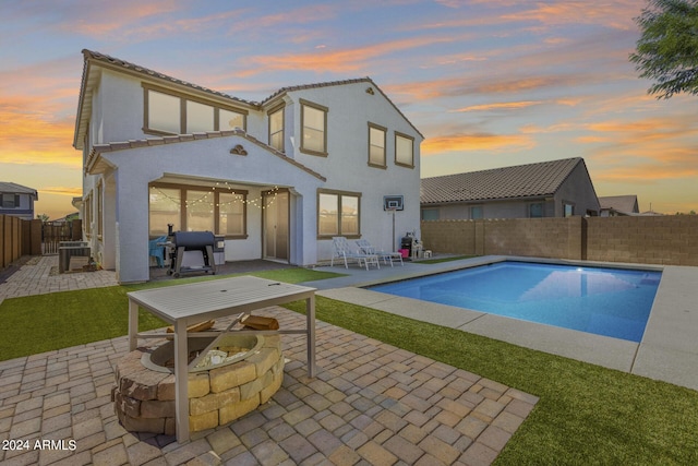 back house at dusk with an outdoor fire pit, an outdoor structure, a fenced in pool, and a patio area