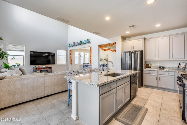 kitchen featuring light tile patterned flooring, sink, gray cabinetry, a center island with sink, and black dishwasher