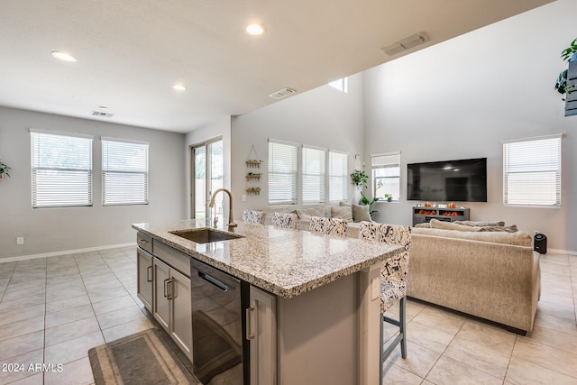 kitchen featuring an island with sink, black dishwasher, sink, light tile patterned floors, and light stone countertops