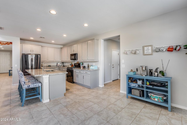 kitchen featuring a kitchen bar, sink, light stone counters, a center island with sink, and black appliances