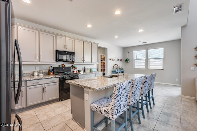 kitchen featuring a kitchen bar, sink, light stone counters, an island with sink, and black appliances