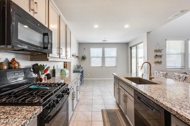 kitchen featuring light stone counters, sink, light tile patterned floors, and black appliances