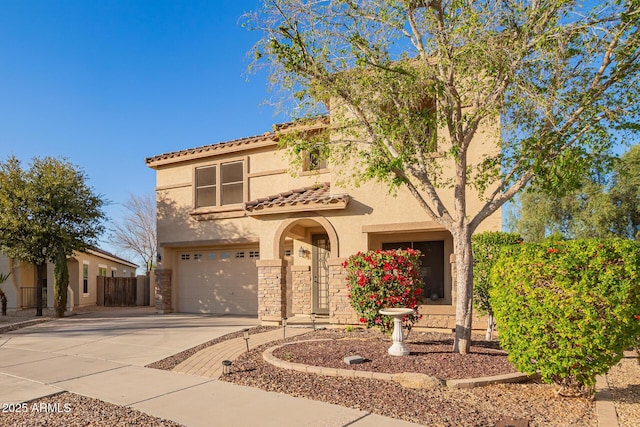 mediterranean / spanish home with a tile roof, concrete driveway, stucco siding, stone siding, and an attached garage