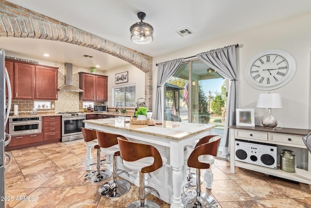 kitchen with tasteful backsplash, visible vents, wall chimney range hood, a kitchen breakfast bar, and stainless steel appliances