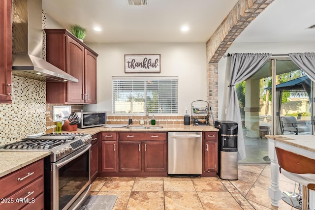 kitchen featuring backsplash, a sink, stainless steel appliances, wall chimney range hood, and a wealth of natural light