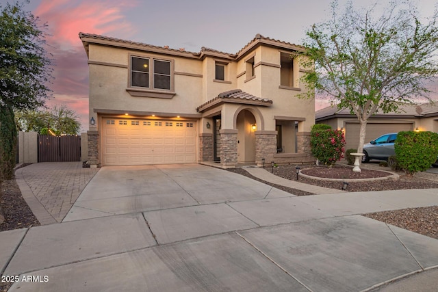 mediterranean / spanish-style home with a gate, stucco siding, concrete driveway, a garage, and stone siding