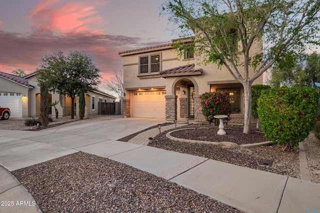 mediterranean / spanish house with stucco siding, stone siding, fence, concrete driveway, and a tiled roof