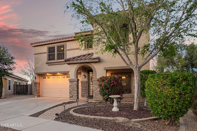 mediterranean / spanish home featuring an attached garage, a tiled roof, stucco siding, stone siding, and driveway