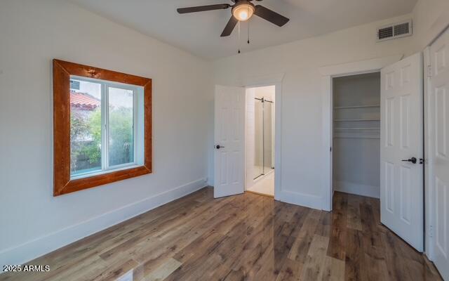 unfurnished bedroom with wood finished floors, a closet, ceiling fan, baseboards, and visible vents